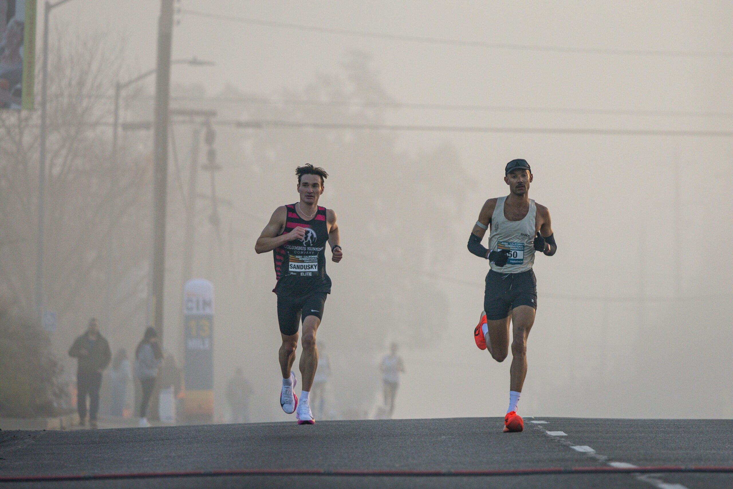 Two marathon runners lead the race on a foggy morning, showcasing athletic endurance.